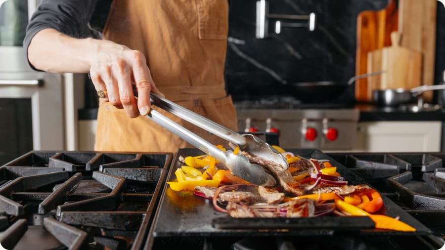 Tongs turning peppers and steak on a griddle