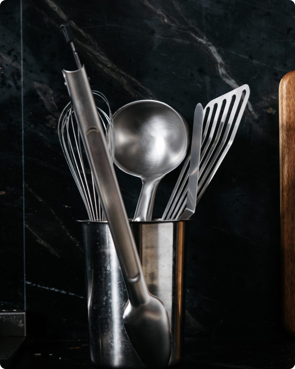 Stainless steel utensils in a holder on a dark marble counter