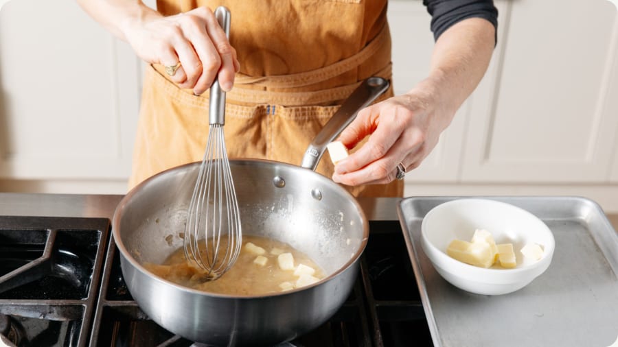 Whisk resting on the rim of a saucepan while adding butter