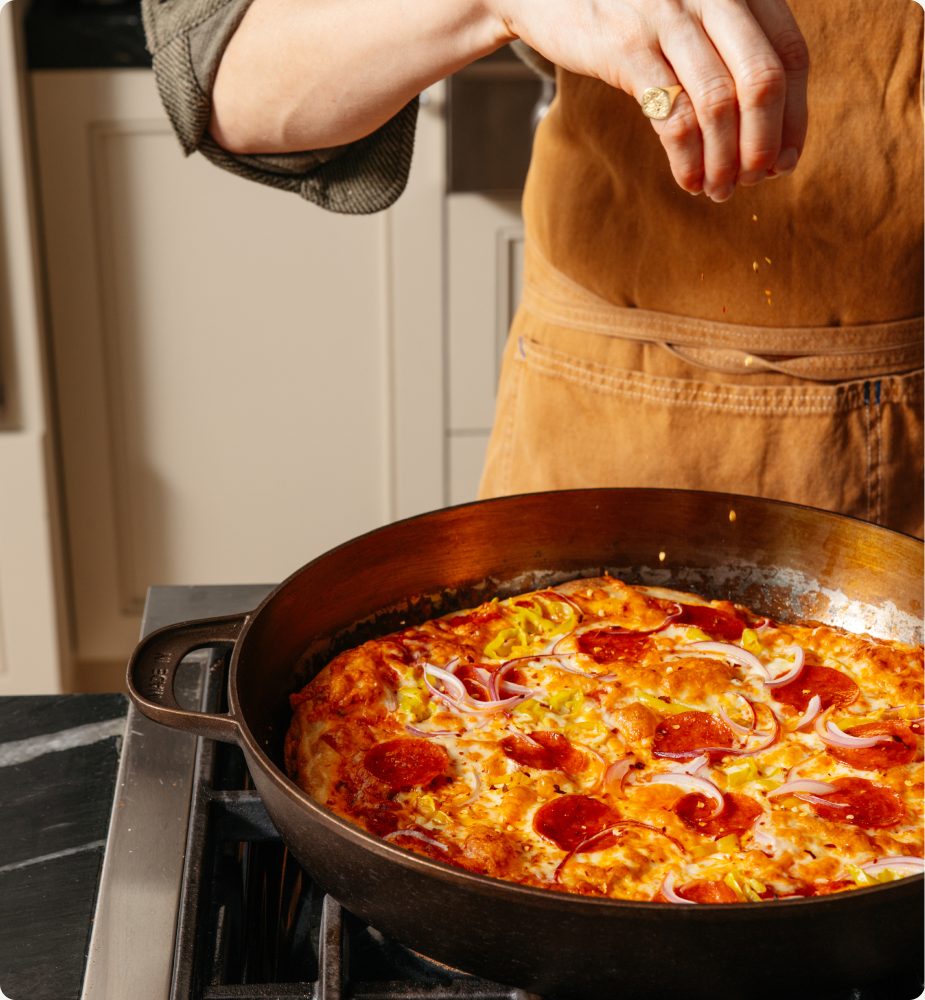 Cast iron pizza with pepperoni and onion on the stovetop