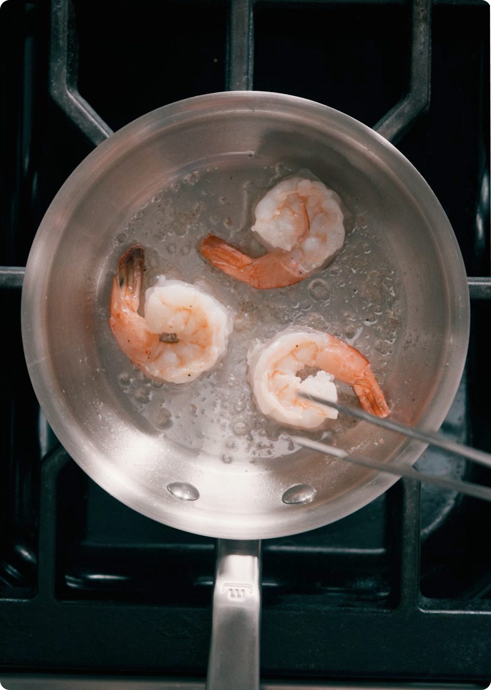 Shrimp cooking in the stainless steel frying pan on a stovetop
