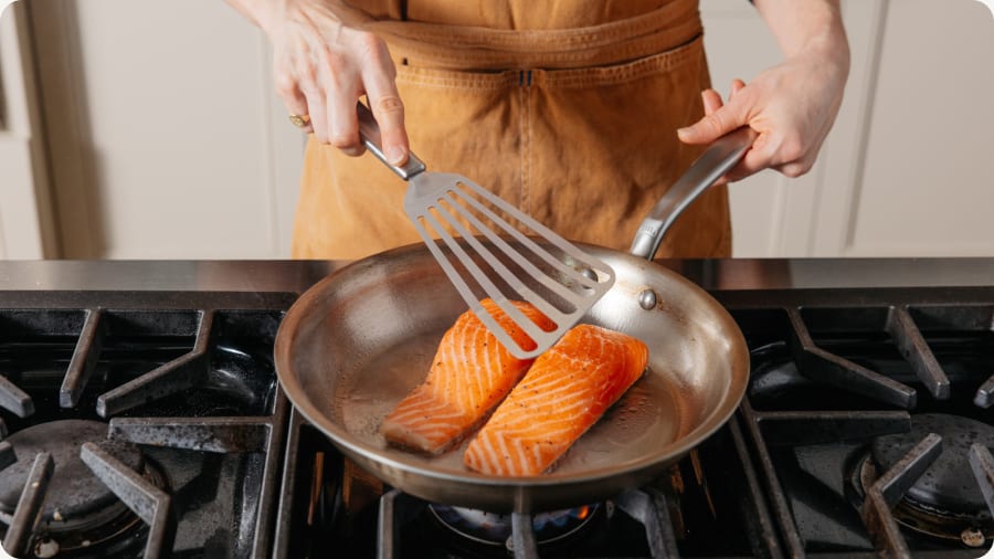 Fish spatula lifting salmon fillets in a frying pan on the stove