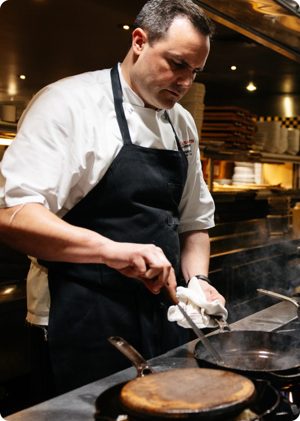 Chef John Kleifgen wiping a cast iron pan in the kitchen at Nick & Sam's