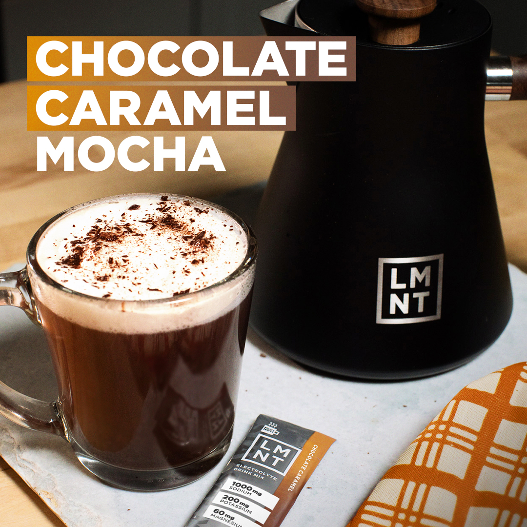 "Chocolate Caramel Mocha" showing a glass mug of frothy mocha topped with chocolate shavings, beside a black LMNT kettle and a Chocolate Caramel LMNT stick pack.