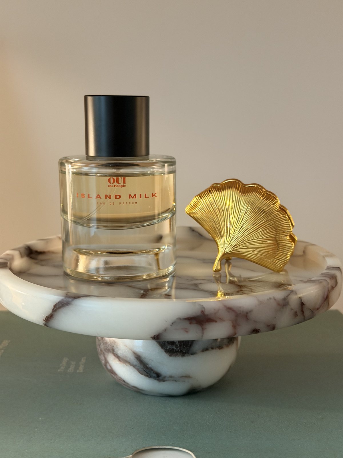 A bottle of Island Milk on a marble stand beside a gold ginkgo leaf