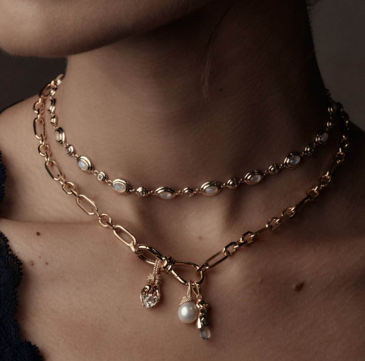 Model wearing layered gold charm necklaces with pearl and crystal charms