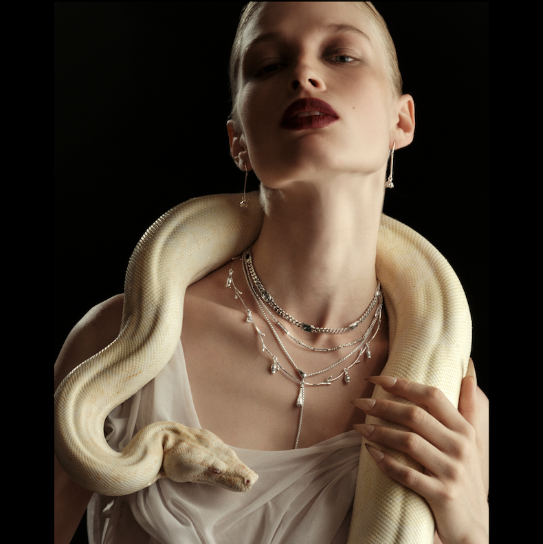 A model in layered silver necklaces holding a white snake
