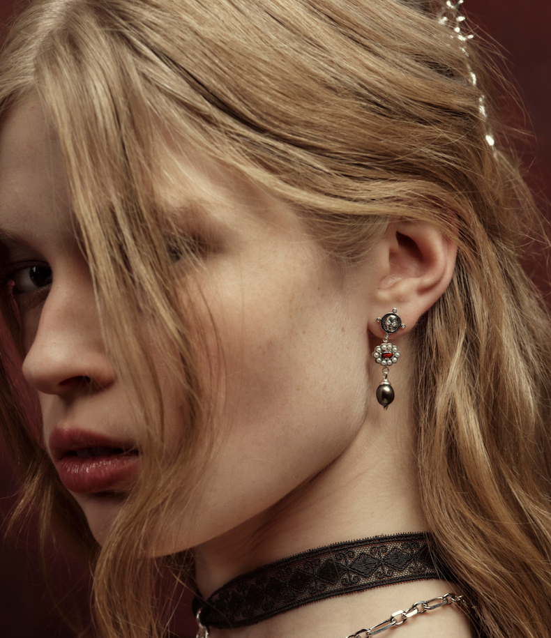 A woman wearing a skull and pearl drop earring and a lace choker