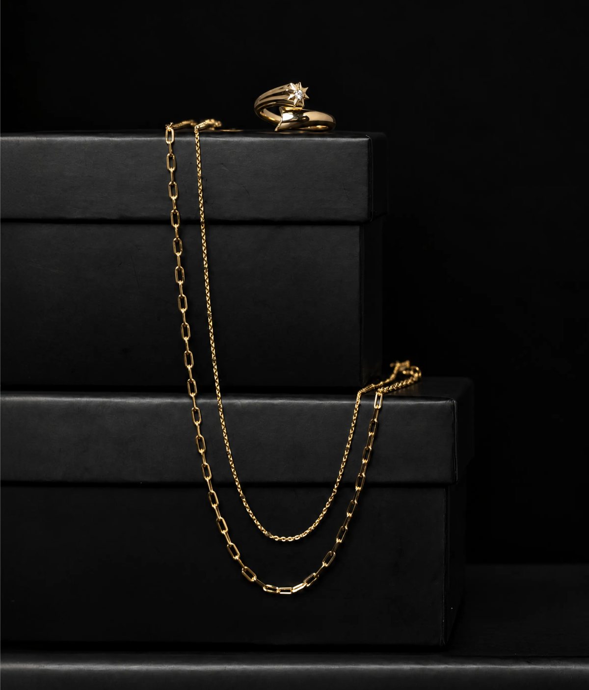 14k gold chains and a star ring on stacked black gift boxes