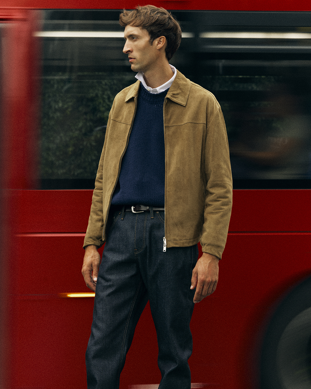 Full body down to knees image of man looking to the left of the image. He wears Super Zero® Hiut jeans, light brown jackets, navy wool jumper over white shirt. 