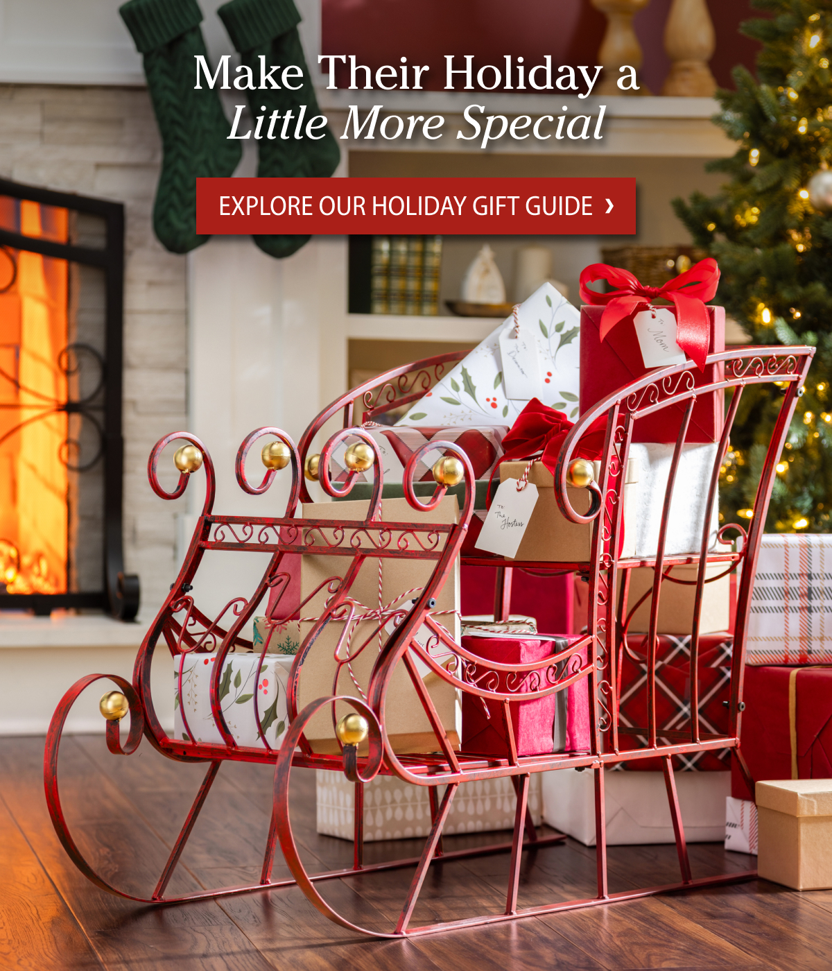 A red decorative sleigh filled with wrapped gifts beside a glowing fireplace and Christmas tree. Text reads: ‘Make Their Holiday a Little More Special’ and ‘Explore Our Holiday Gift Guide.'