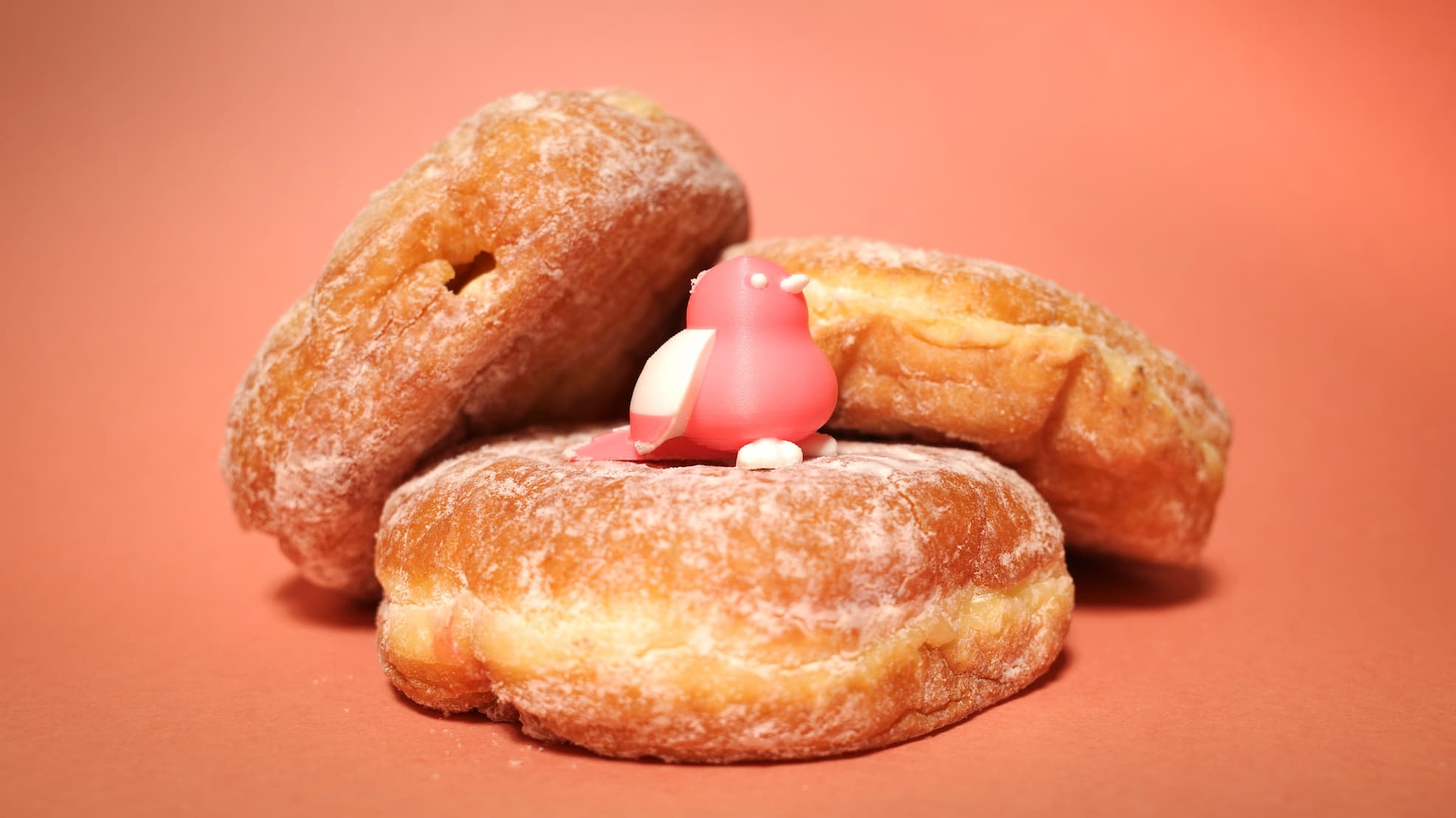 A small pink bird perched on a stack of powdered donuts.