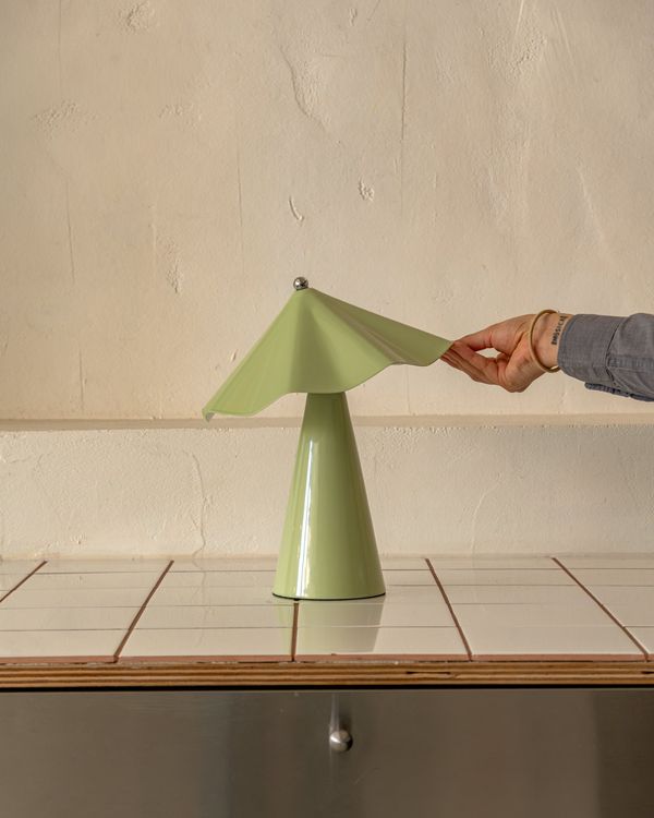 A hand tilting the shade of a Pistachio Robyn lamp