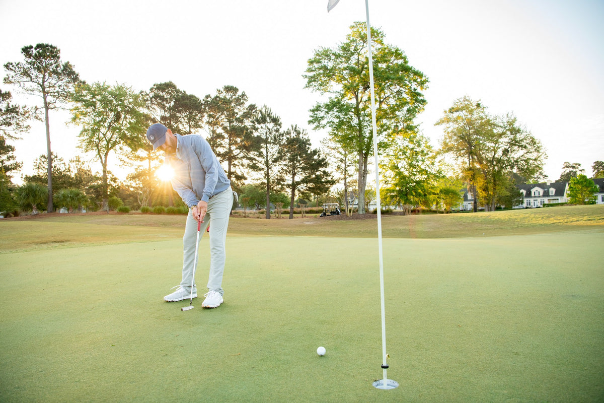 A golfer on a sunlit green, with rolling countryside beyond