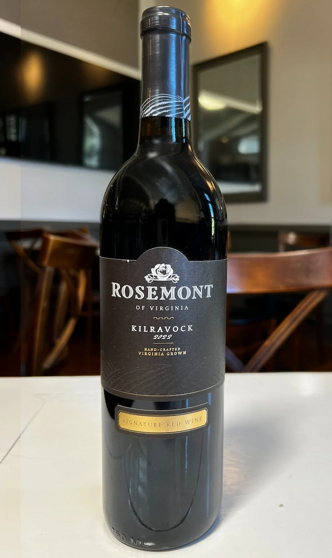 Bottle of Rosemont of Virginia Kilravock 2022 Signature Red Wine, featuring a black and gold label, displayed on a white table in a warmly lit dining room. Fearrington Village.