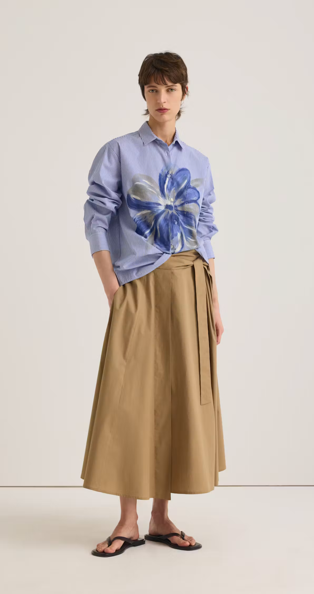 Model wearing a blue striped shirt with an oversized blue floral print, paired with a tan midi skirt and black sandals. Fearrington Village.
