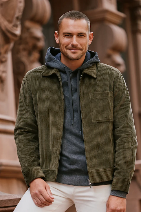 Man wearing an olive corduroy jacket layered over a charcoal hoodie with cream trousers. Fearrington Village.
