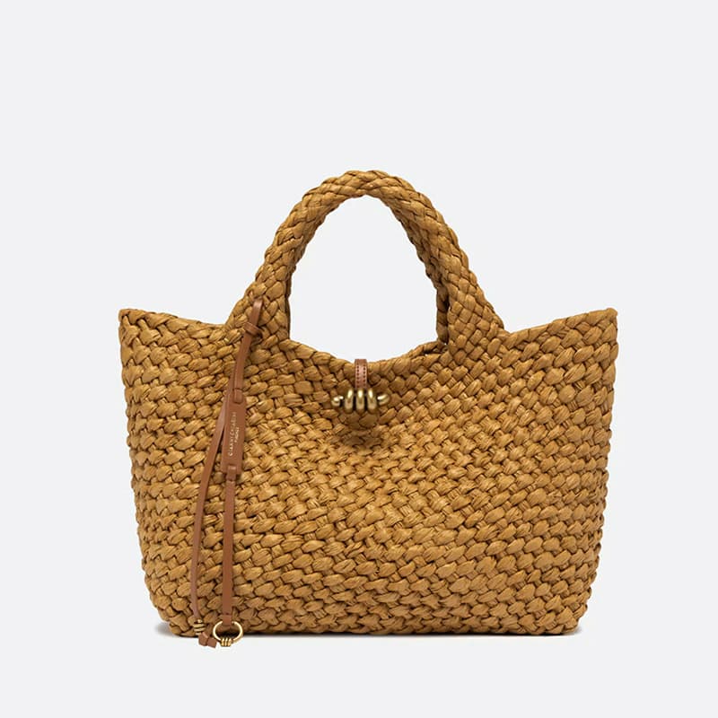 Large handwoven tan tote with chunky braided handles, leather tie details, and gold-tone hardware. Fearrington Village.