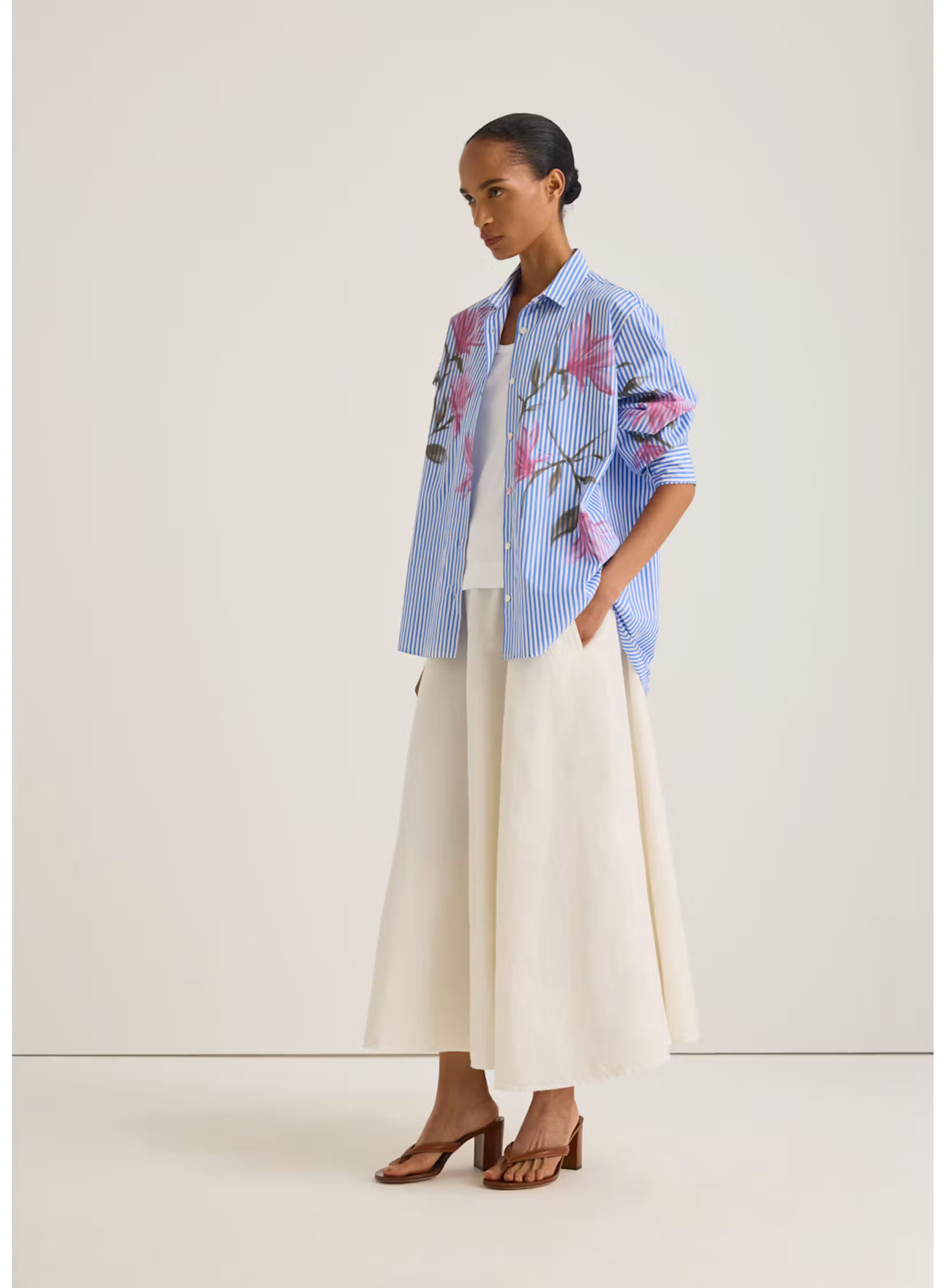 Model wearing an oversized blue-and-white striped shirt with a pink floral print, paired with a flowing ivory midi skirt and brown heeled sandals. Fearrington Village.