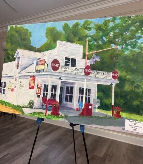 Painting of a vintage country store and gas station with Coca-Cola signs and red gas pumps, displayed on an easel. Fearrington Village.