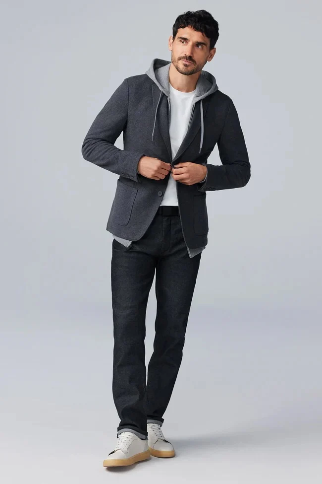 Man wearing a charcoal blazer layered over a gray hoodie and white T-shirt with dark jeans and white sneakers. Fearrington Village.