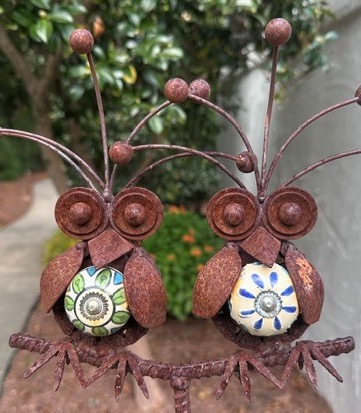 Two whimsical rusted metal owl sculptures with colorful ceramic tile bellies perched together on a branch. Fearrington Village.