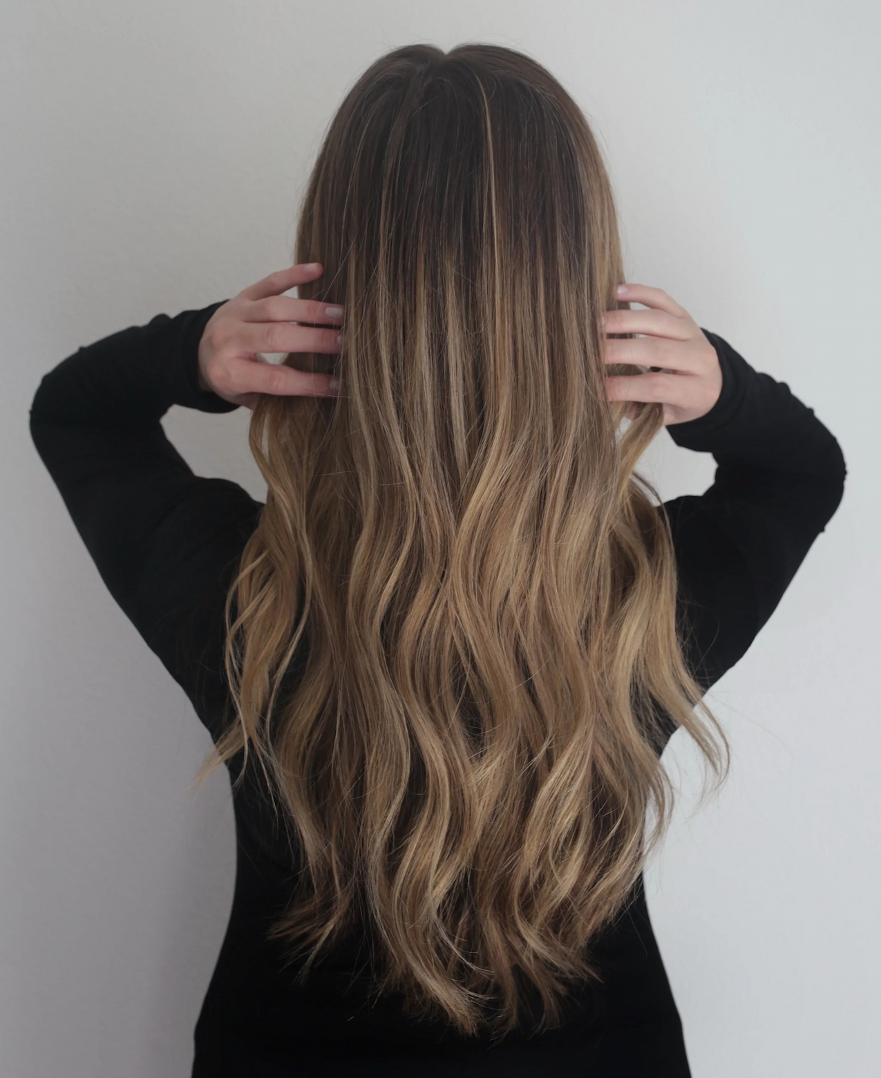 Back view of long, softly waved brunette hair with warm blonde highlights and natural dimension. Fearrington Village.