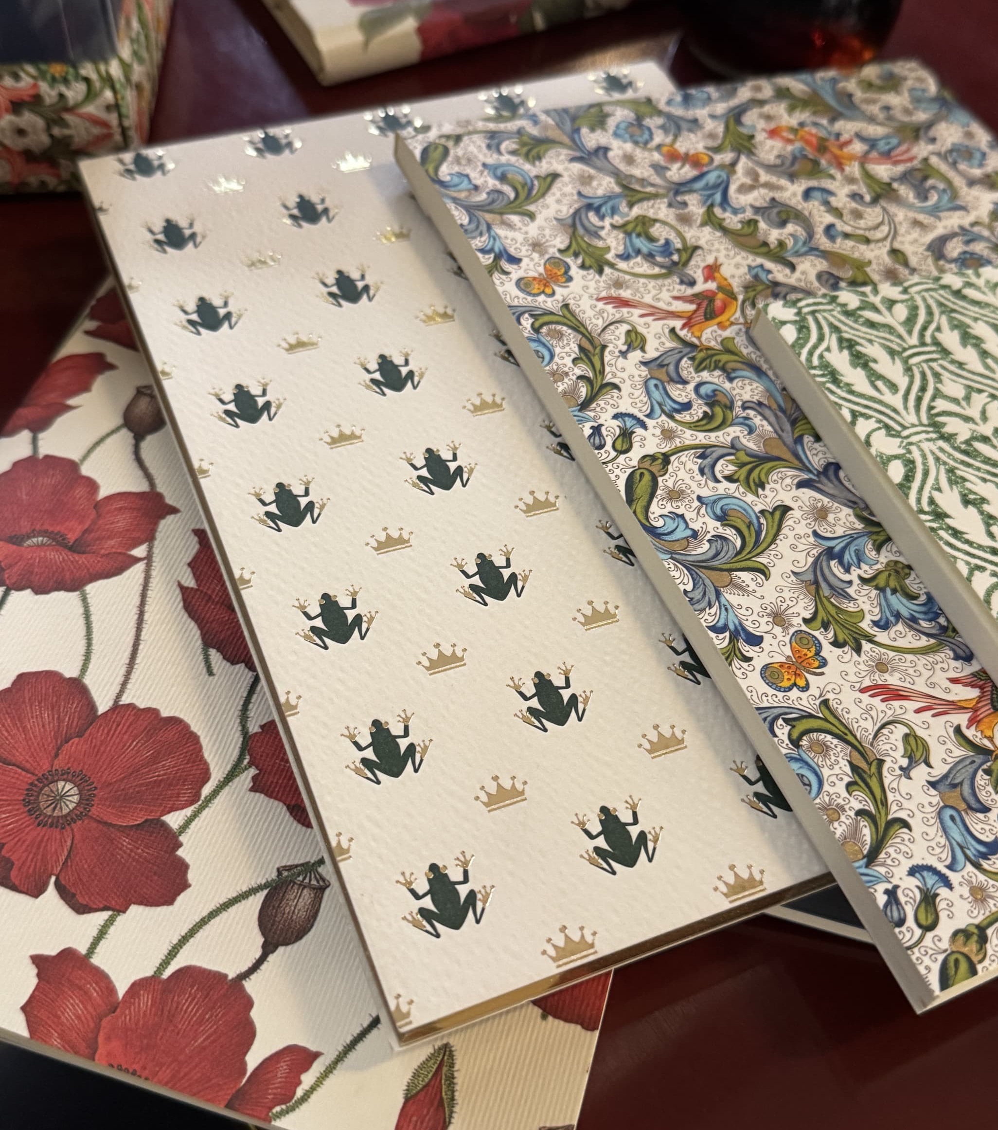 Decorative stationery and notebooks layered in floral, frog-and-crown, and intricate botanical patterns. Fearrington Village.