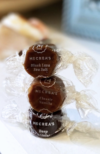 Three individually wrapped McCrea’s Candies caramels stacked together in Black Lava Sea Salt, Classic Vanilla, and Deep Chocolate flavors. Fearrington Village.