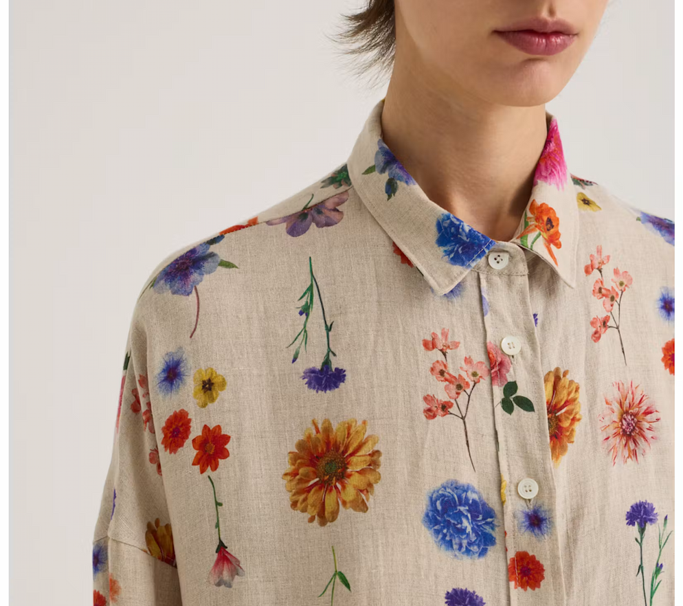 Relaxed button-front shirt in natural linen with a colorful allover floral print in pink, orange, blue, purple, and yellow. Fearrington Village.