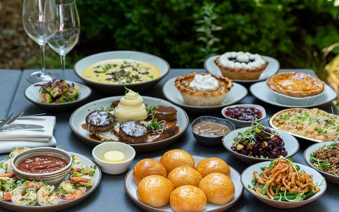 An elegant Thanksgiving feast from Fearrington featuring roasted meats, creamy mashed potatoes, shrimp, golden Parker House rolls, seasonal vegetables, savory casseroles, cranberry sauce, and assorted holiday desserts, beautifully arranged on an outdoor table. Fearrington Village.