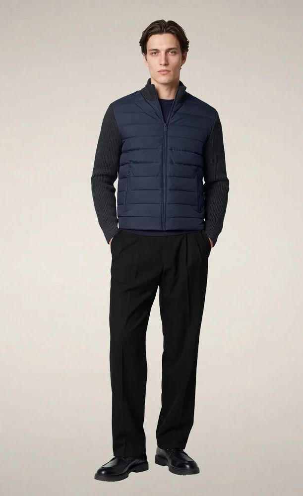 Model wearing a navy quilted zip-front jacket with dark ribbed knit sleeves, paired with black tailored trousers and black leather shoes. Fearrington Village.