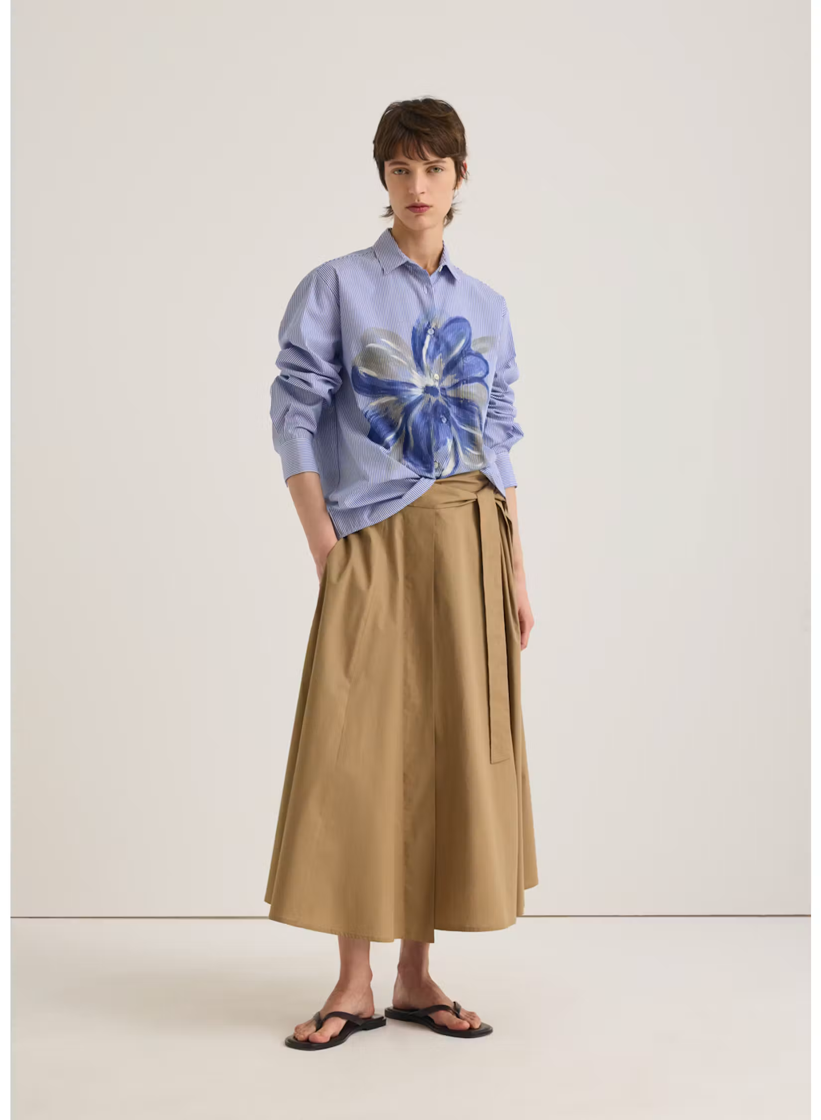 Model wearing a blue striped shirt with an oversized blue floral print, paired with a tan midi skirt and black sandals. Fearrington Village.