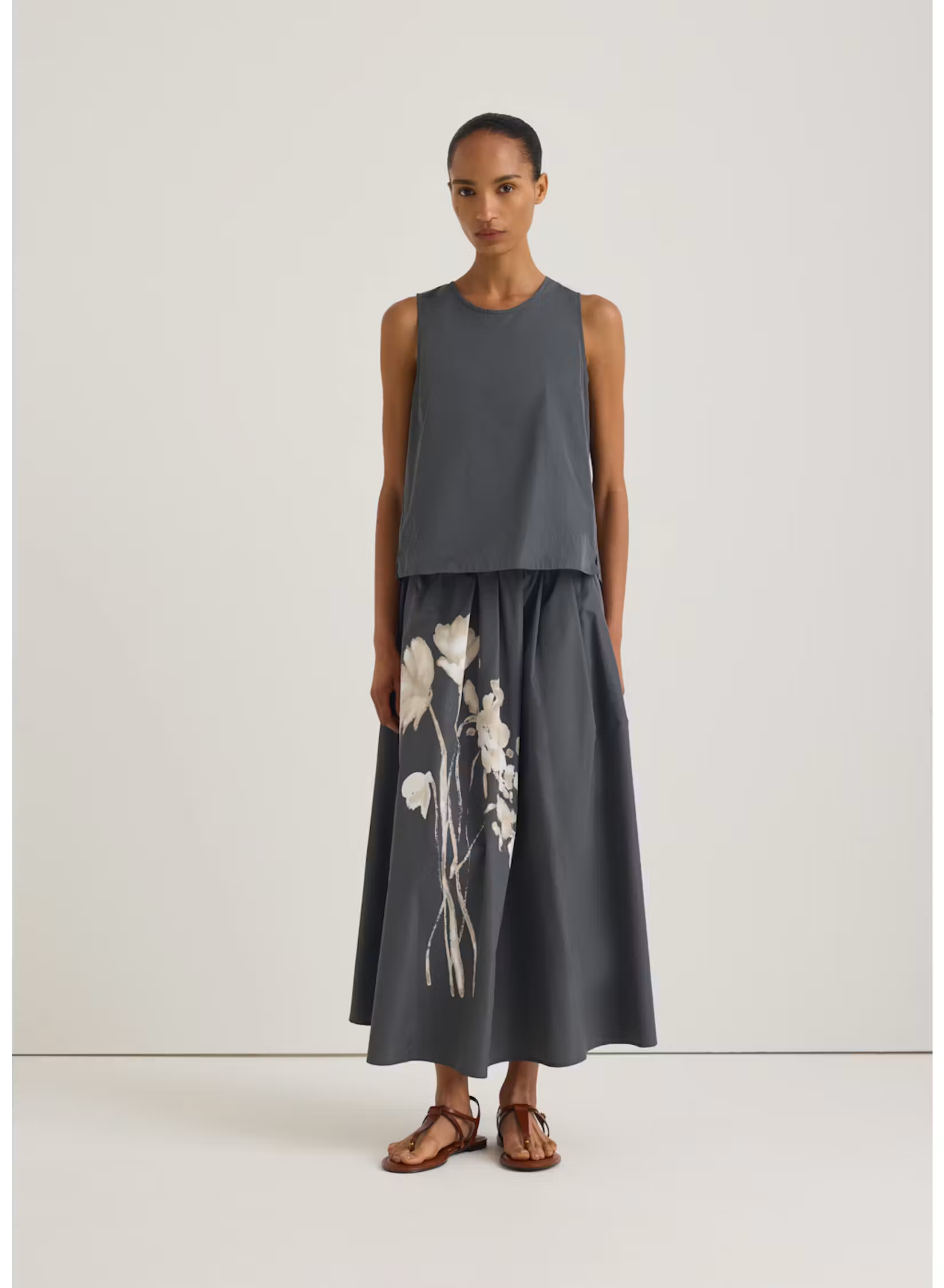 Model wearing a charcoal sleeveless top with a matching full midi skirt featuring a large white floral print. Fearrington Village.