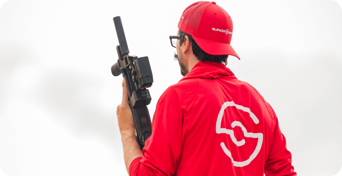 Shooter in red jacket and cap holding rifle.
