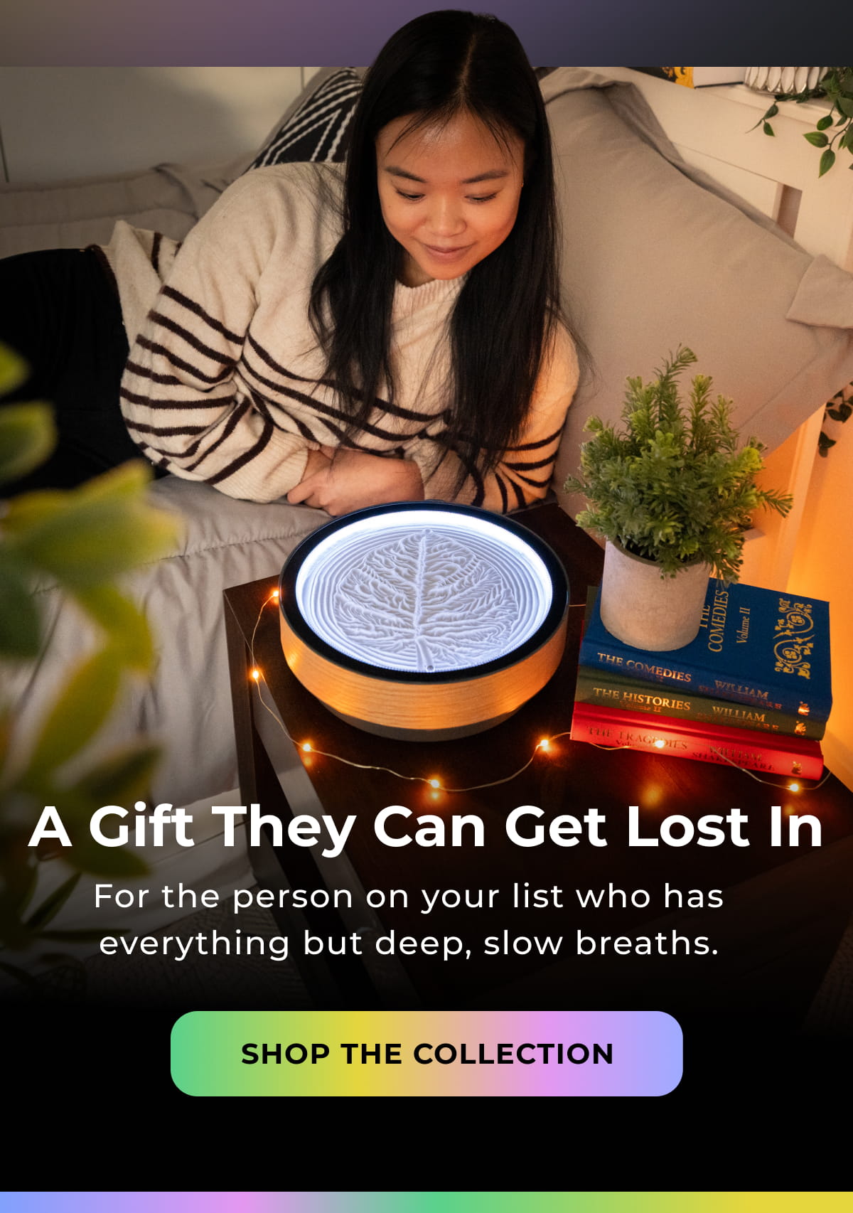 Woman relaxing beside a glowing Oasis Mini with books and lights.