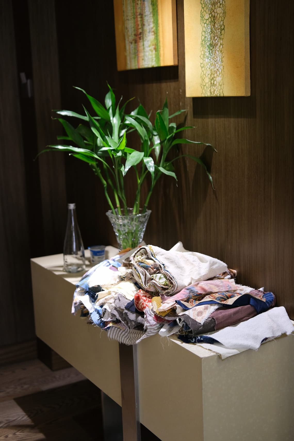 A pile of fabric samples on a console table beside a potted plant