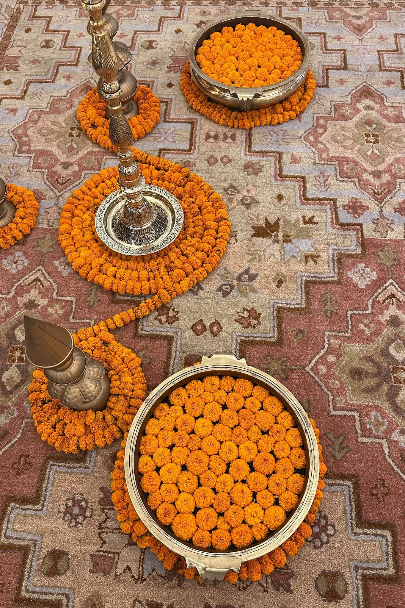 Marigold garlands and brass bowls arranged on a patterned rug