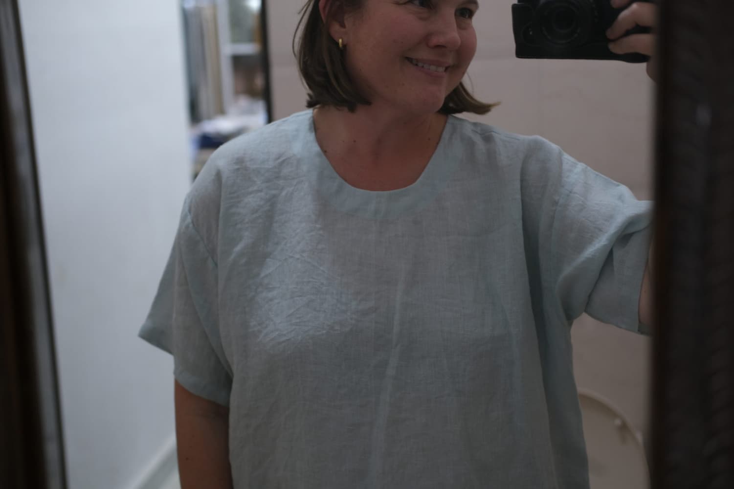 Emily trying on a pale blue linen shirt sample in a mirror