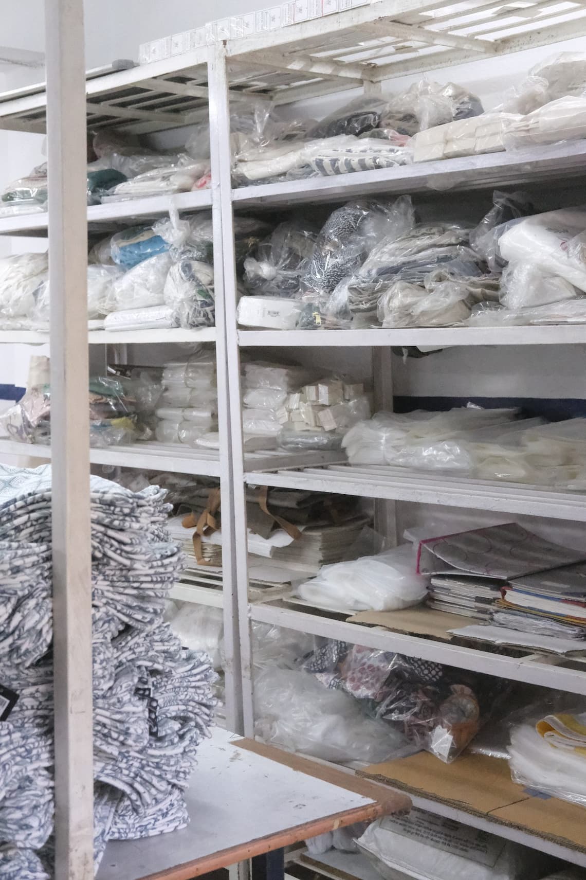 Metal shelves stacked with folded cloth and garments in a workroom