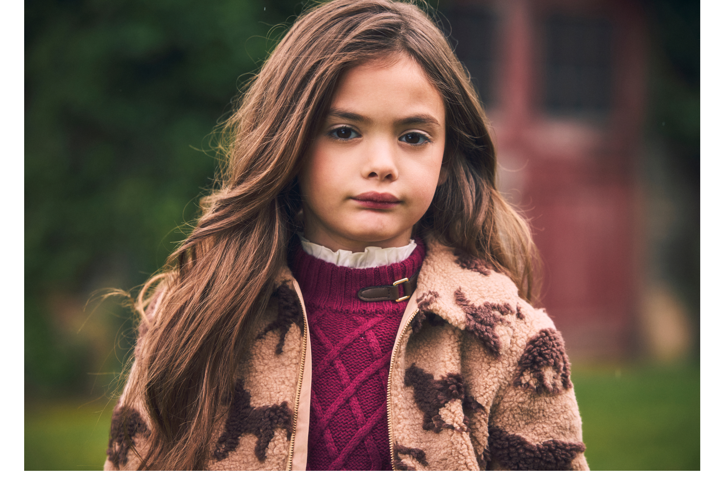 Young girl wearing a sherpa horse-print jacket over a cable-knit burgundy sweater