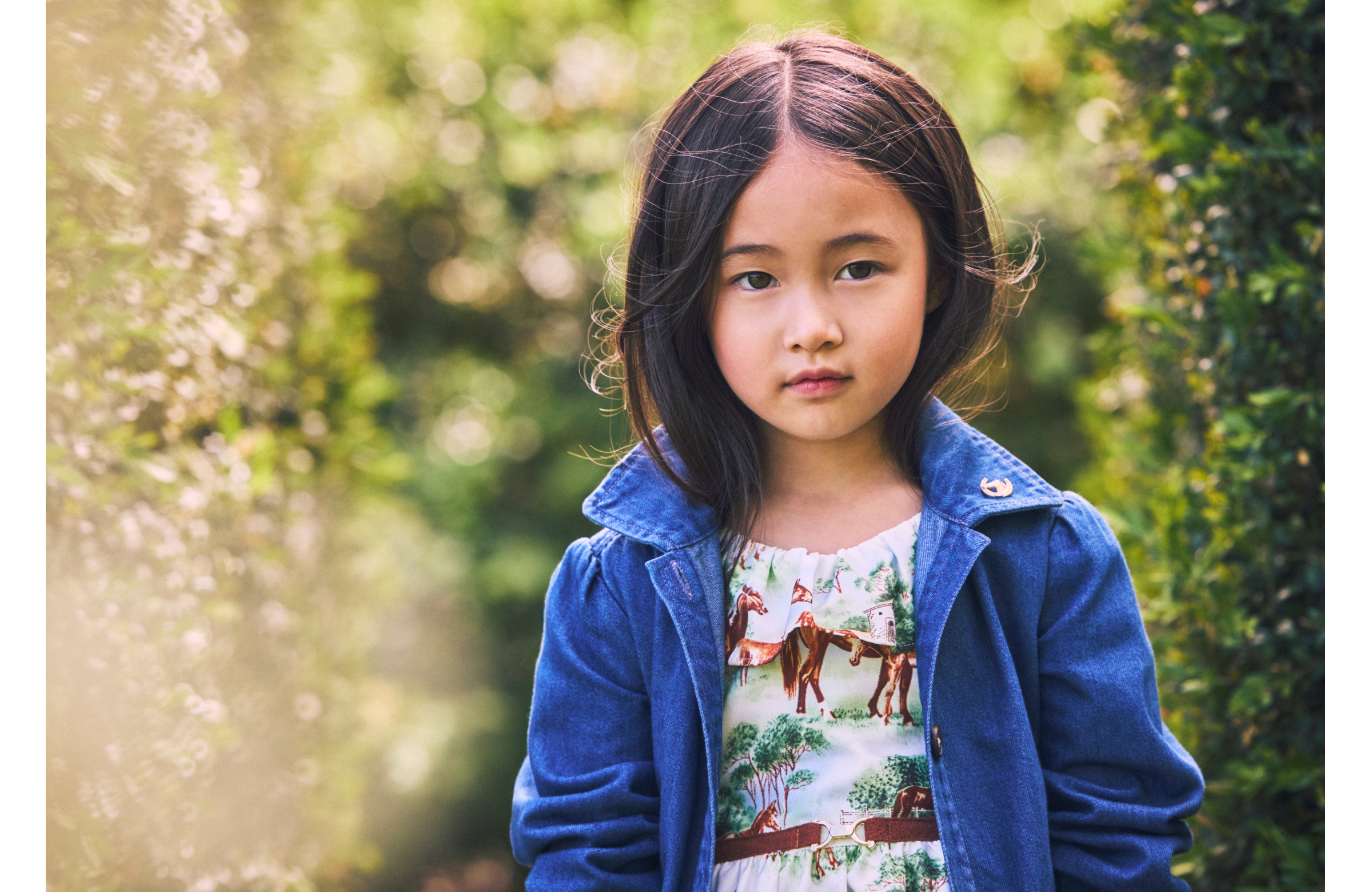 Young girl in denim jacket and horse-print dress standing outdoors