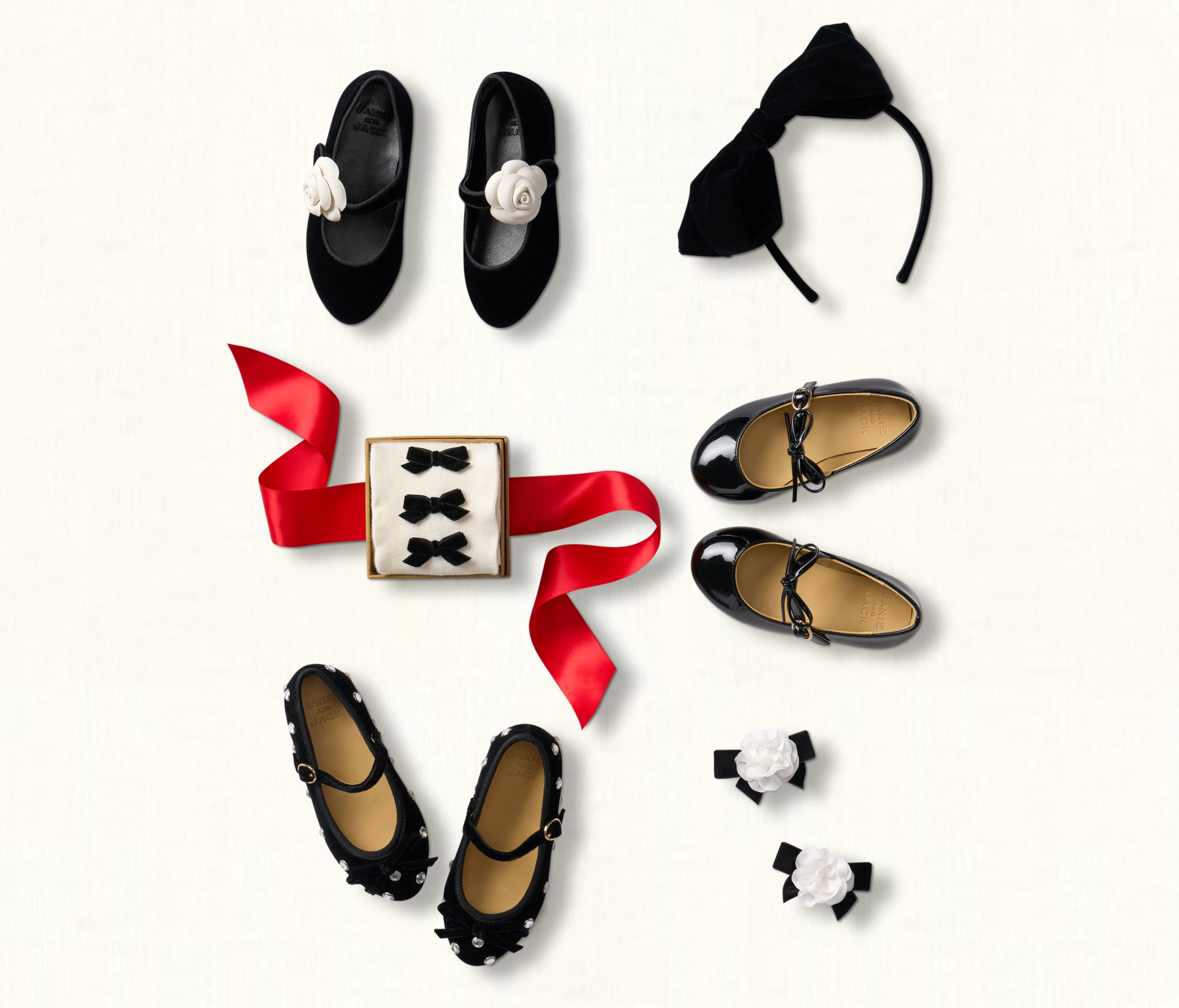 Flatlay of children's black Mary Jane shoes, hair accessories, and velvet bows with red ribbon