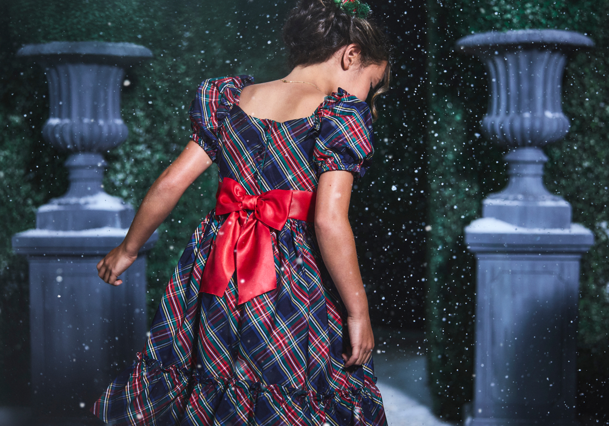 Girl in tartan plaid dress with red satin bow twirling in the snow