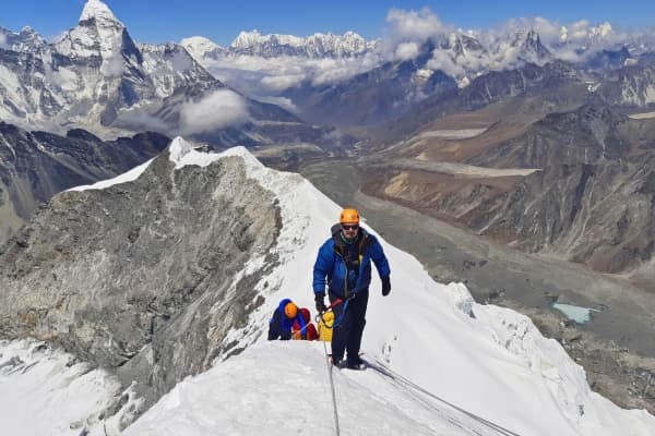 Hikers on a snowy ridge with snowy mountains in the background