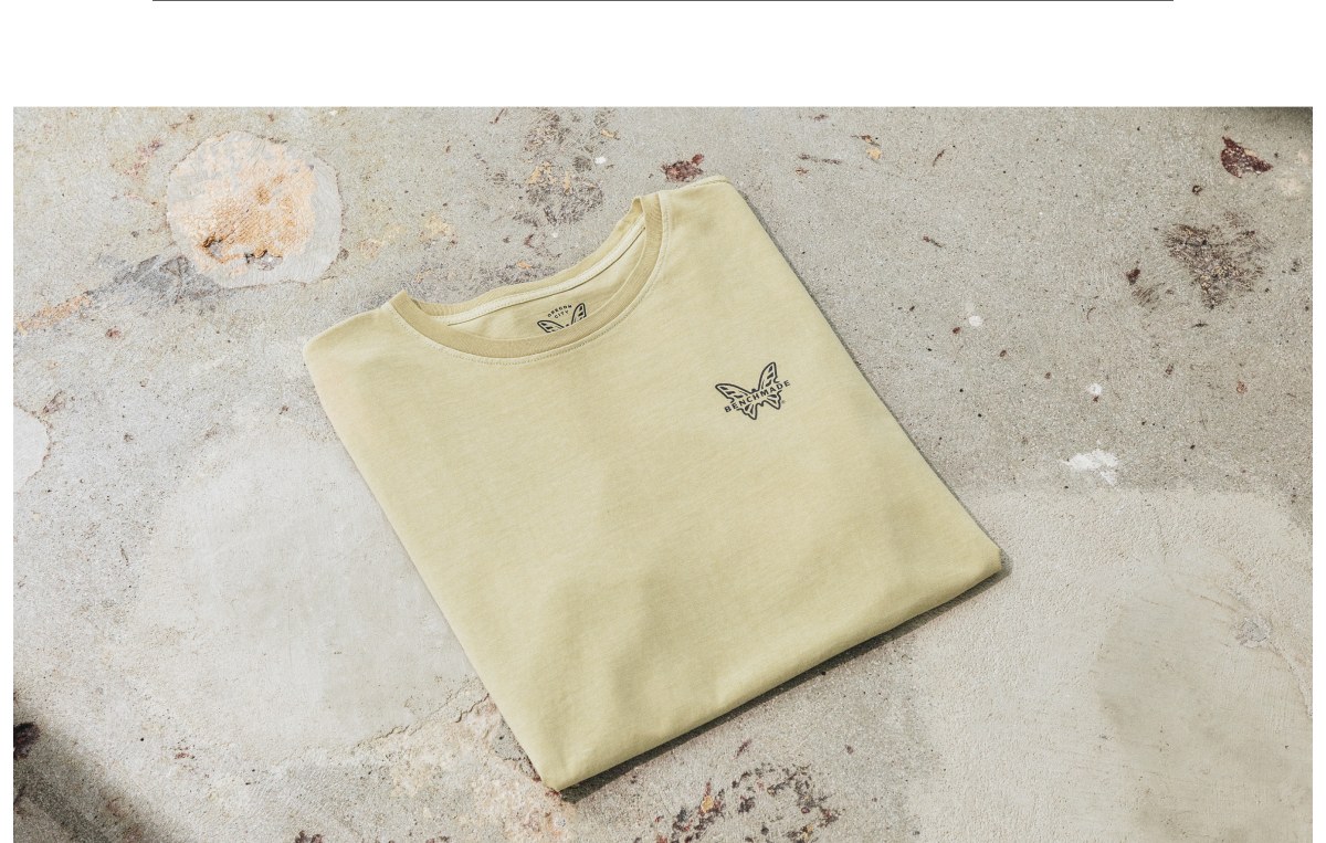 Butterfly graphic on a light yellow t-shirt laid flat on a textured surface.