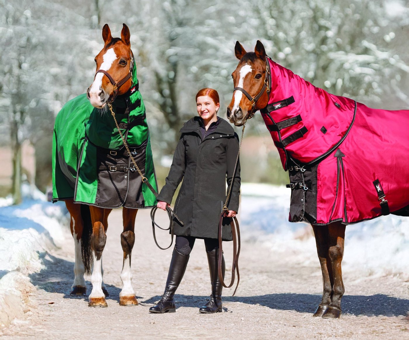 Two horses in green and red StormShield turnouts with a rider on a snowy lane