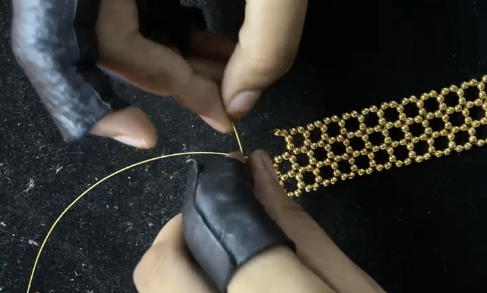 Artisan's hands threading small gold beads onto wire by hand