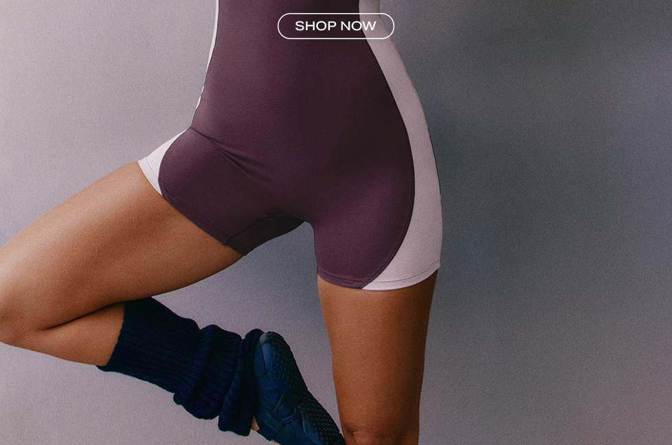 Plum and pink color-blocked activewear romper paired with navy leg warmers, featuring a shop now button to promote new workout apparel.