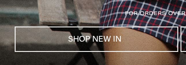 Close-up of a person sitting on a wooden bench wearing a blue and red plaid skirt, featuring a Shop New In banner for new fashion arrivals.
